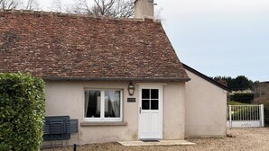 Een klein huis met pannendak, een witte deur en een bordje met de tekst 'Le Petit Gîte'.