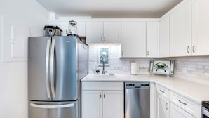 A modern kitchen with stainless steel appliances, white cabinetry, and a marble backsplash.