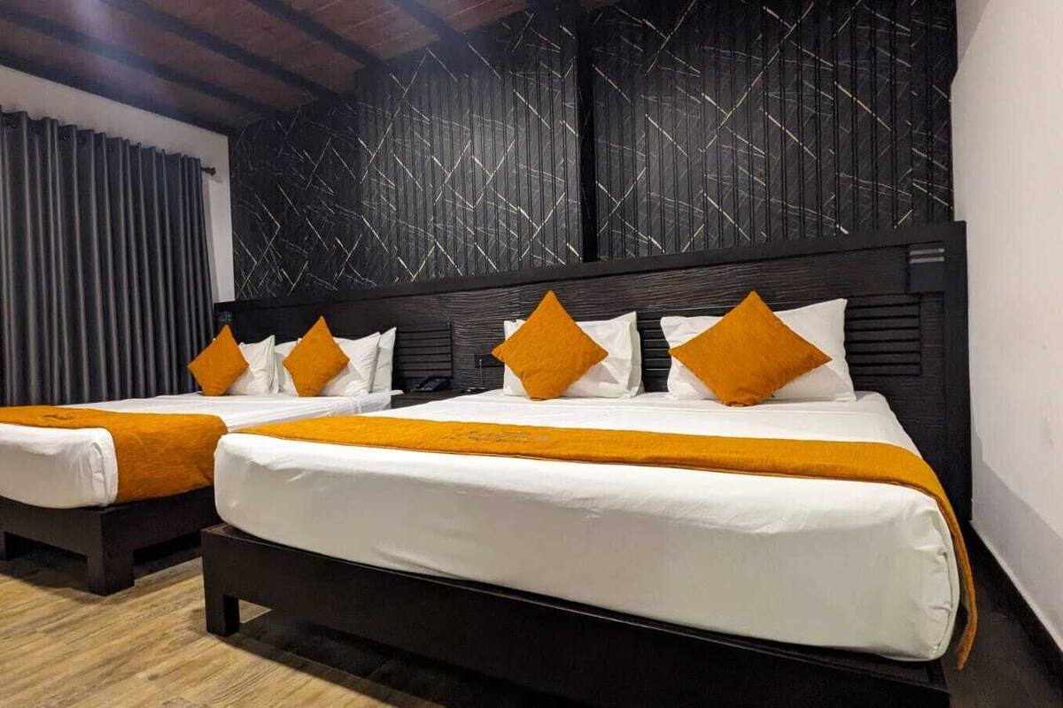 Een hotelkamer met twee bedden, elk met witte beddengoed en oranje accenten. De kamer heeft een donker houten hoofdbord en een behang met een patroon.