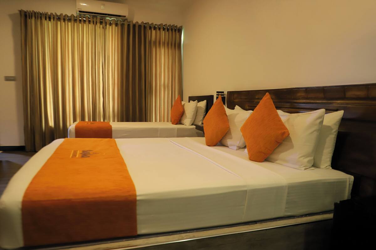 Een hotelkamer met twee bedden, elk met witte beddengoed en oranje accenten, een houten hoofdbord en een groot raam met gordijnen.