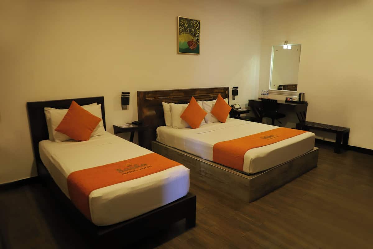 Twee tweepersoonsbedden met oranje beddengoed, een bureau, een stoel en een spiegel in een hotelkamer.