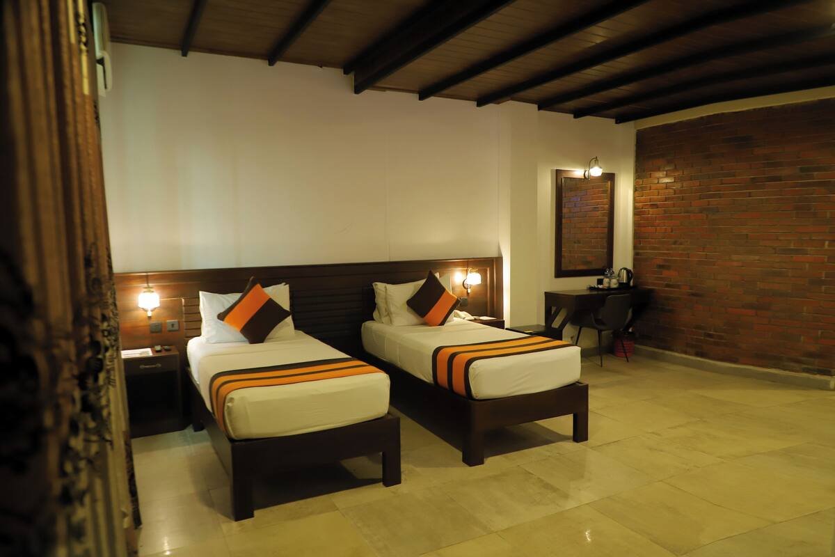 Een hotelkamer met twee bedden, een bakstenen muur en een bureau met een stoel.