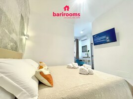 Camera d'albergo con un letto, cuscini, asciugamani, una scrivania e una televisione.