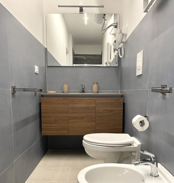 A modern bathroom with a wooden vanity, a toilet, a sink, and a mirror. - Barirooms - Murat Suites (Bari)