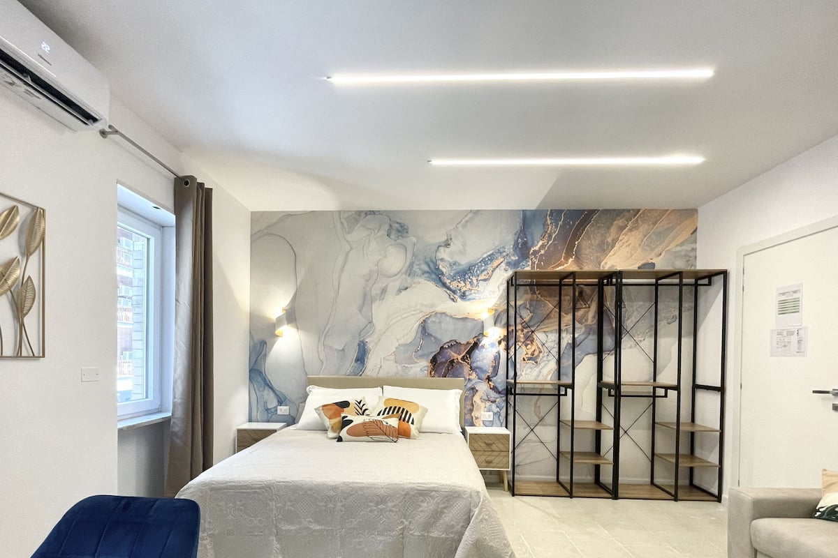 A modern bedroom with a bed, a nightstand, a wall-mounted shelf, and a wardrobe.