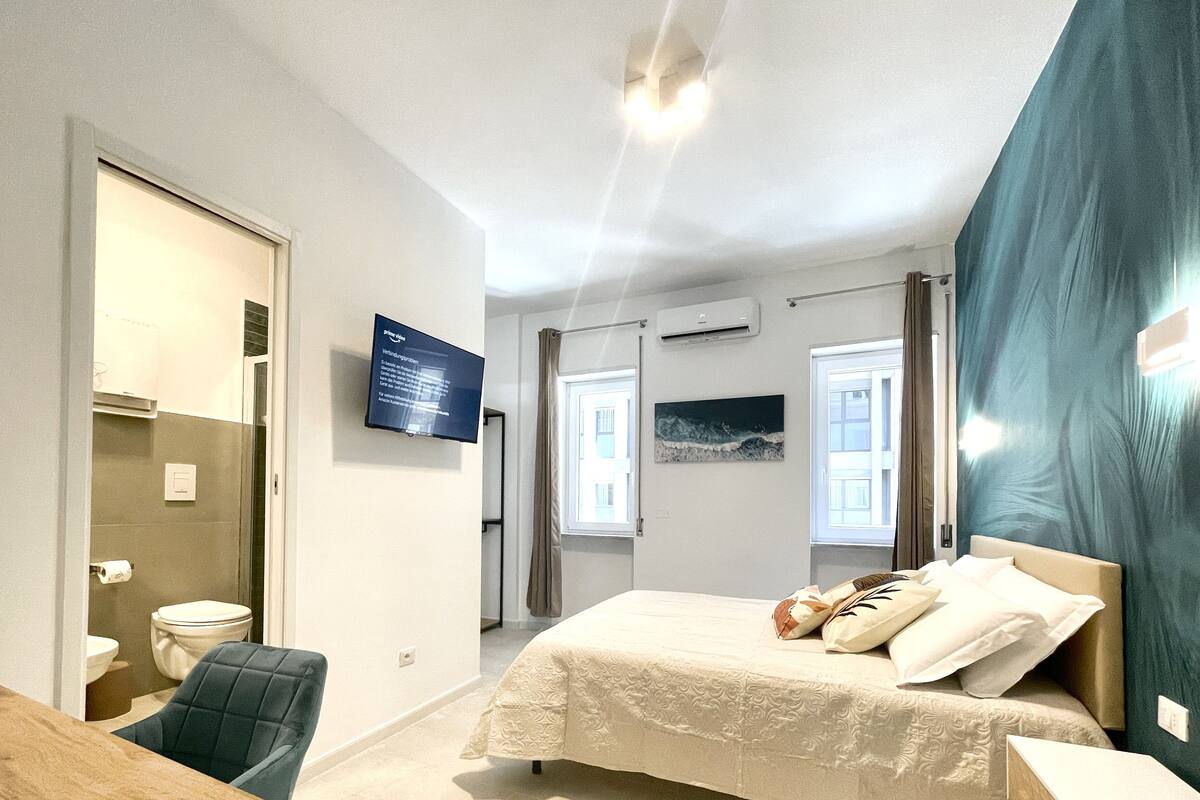 A bedroom with a bed, a chair, a desk, a TV, and a bathroom.