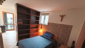Une chambre à coucher avec un lit, une bibliothèque en bois, une petite table et un crucifix fixé au mur.
