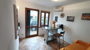 Un espace de vie compact comprenant une table à manger en verre, un canapé, un fauteuil et un petit coin cuisine.