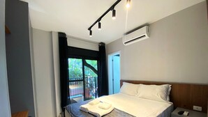 Ein modernes Hotelzimmer mit einem großen Bett, einem Nachttisch, einem Schreibtisch und einem Balkon mit Blick auf Bäume.