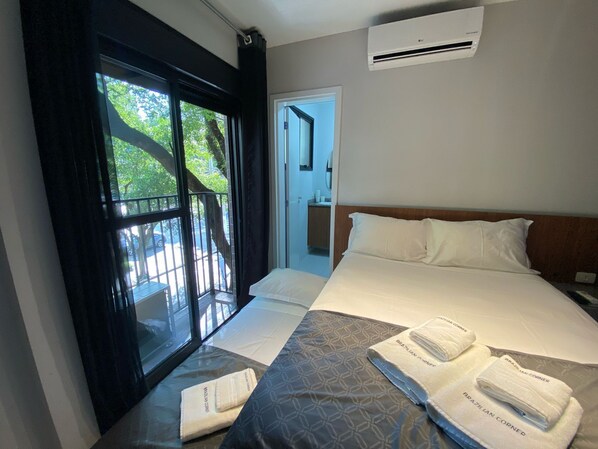 Habitación de hotel con cama, ventana con vistas a árboles y equipo de aire acondicionado en la pared.
