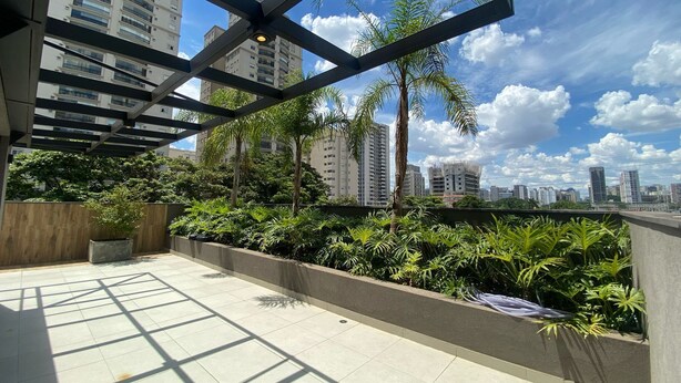 Eine Dachterrasse mit Blick auf eine Stadtlandschaft, umgeben von Grünpflanzen und einer Metallkonstruktion.