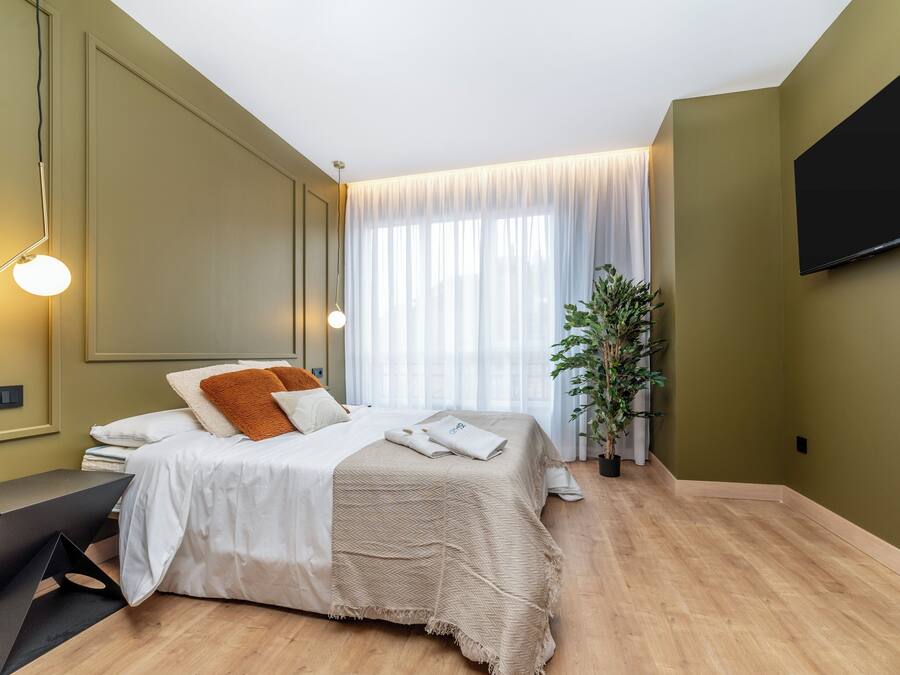 Quarto moderno com cama, mesa de cabeceira e uma janela grande com cortinas.