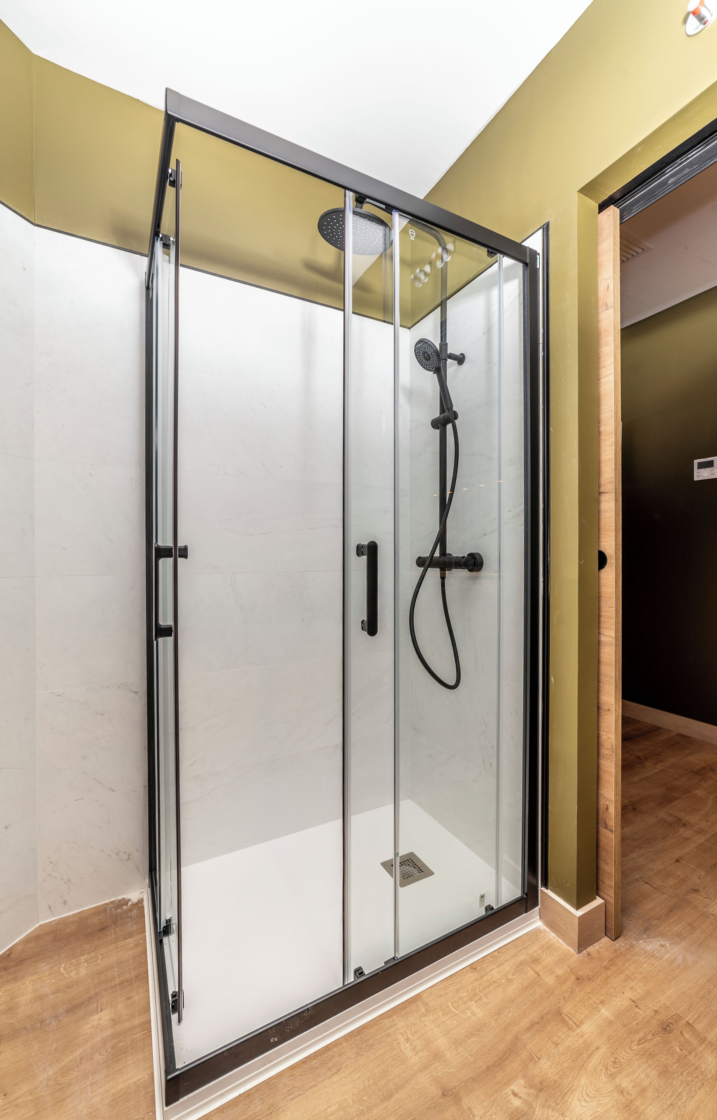 A glass-enclosed shower with a showerhead and control panel.