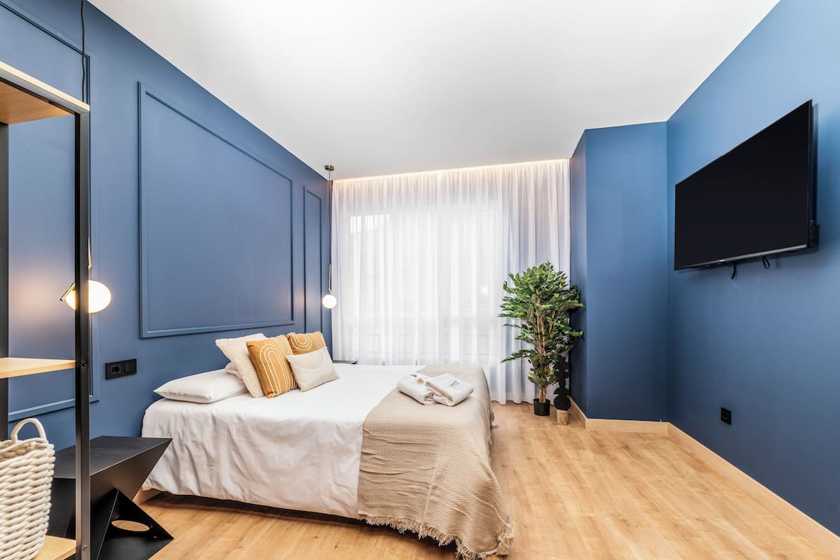 Une chambre à coucher moderne avec un lit, une table de chevet et un téléviseur fixé au mur.