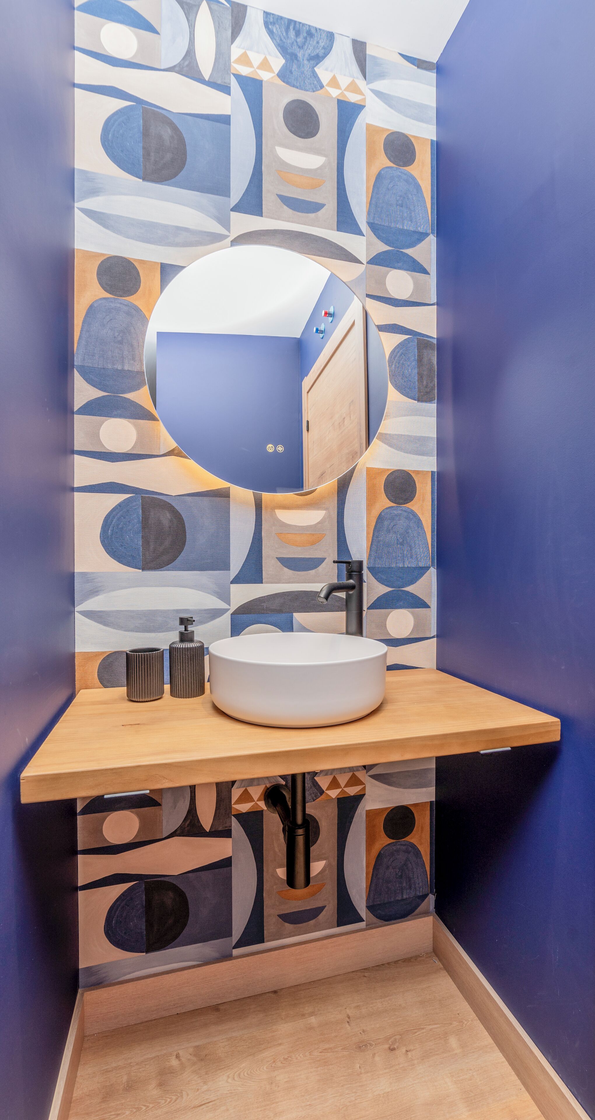 A bathroom with a modern design, featuring a sink, mirror, and a wall with abstract patterns.