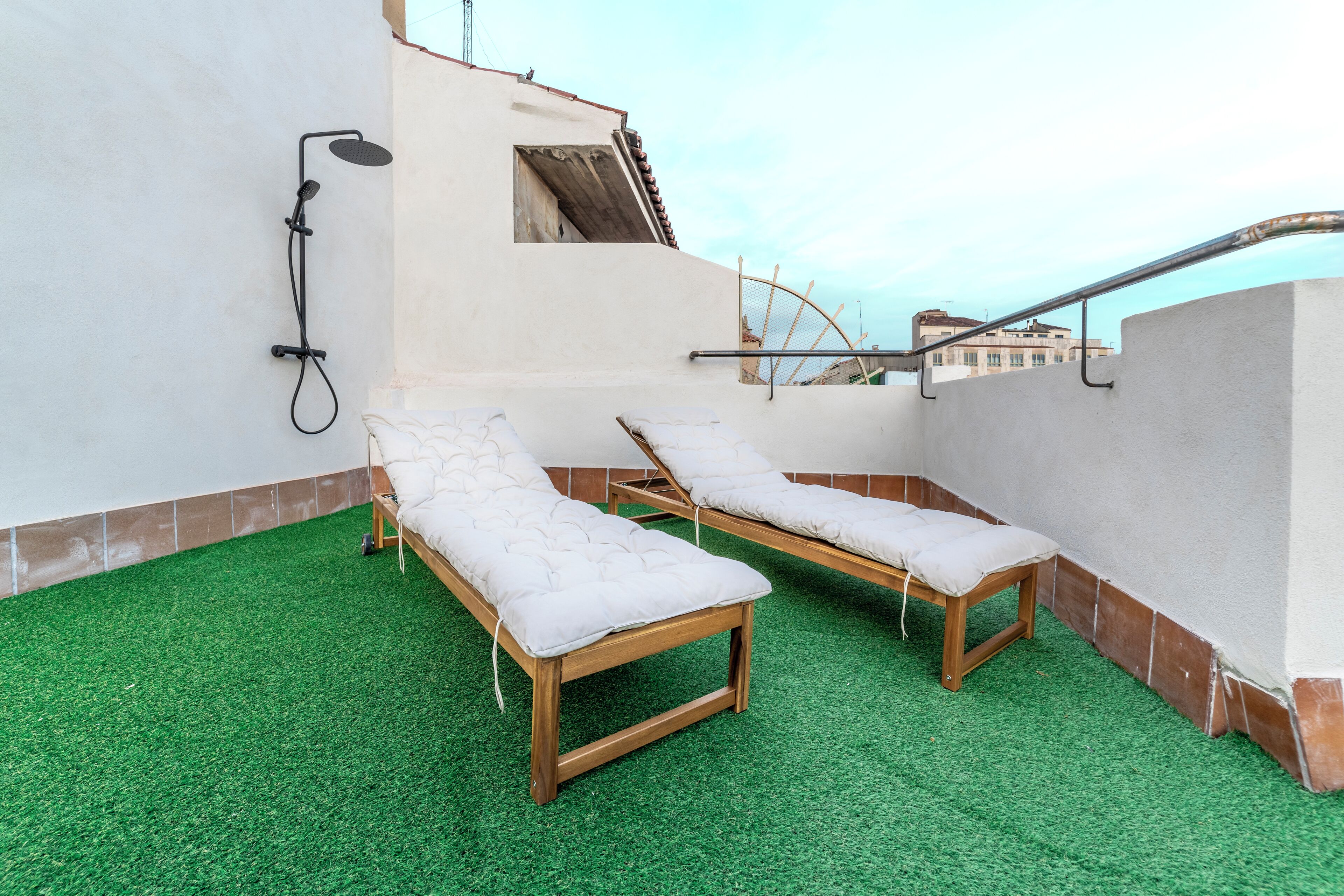 A rooftop terrace with two wooden sun loungers and a built-in shower.
