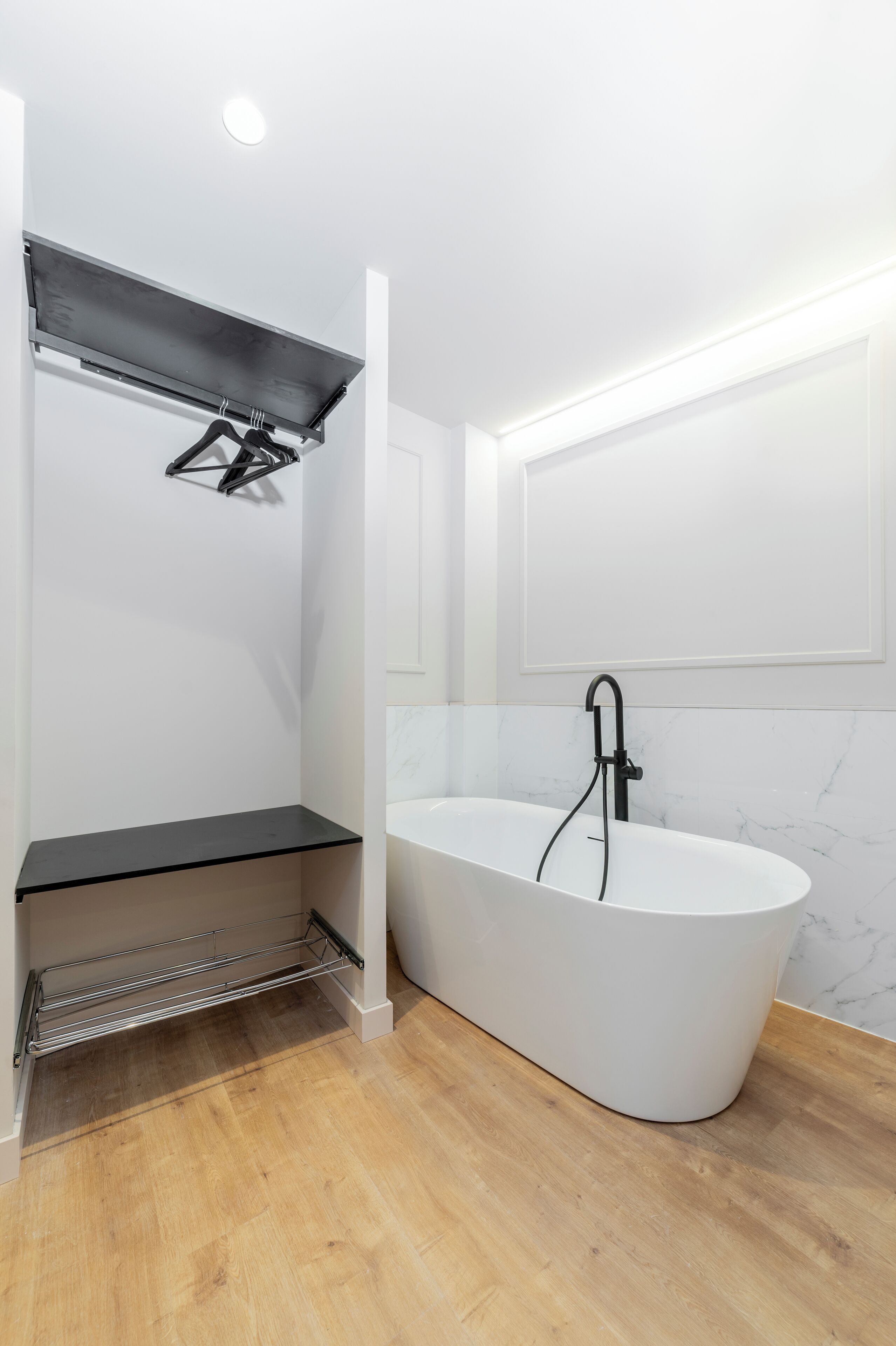 A modern bathroom with a freestanding bathtub, a metal shelf, and a white marble wall.