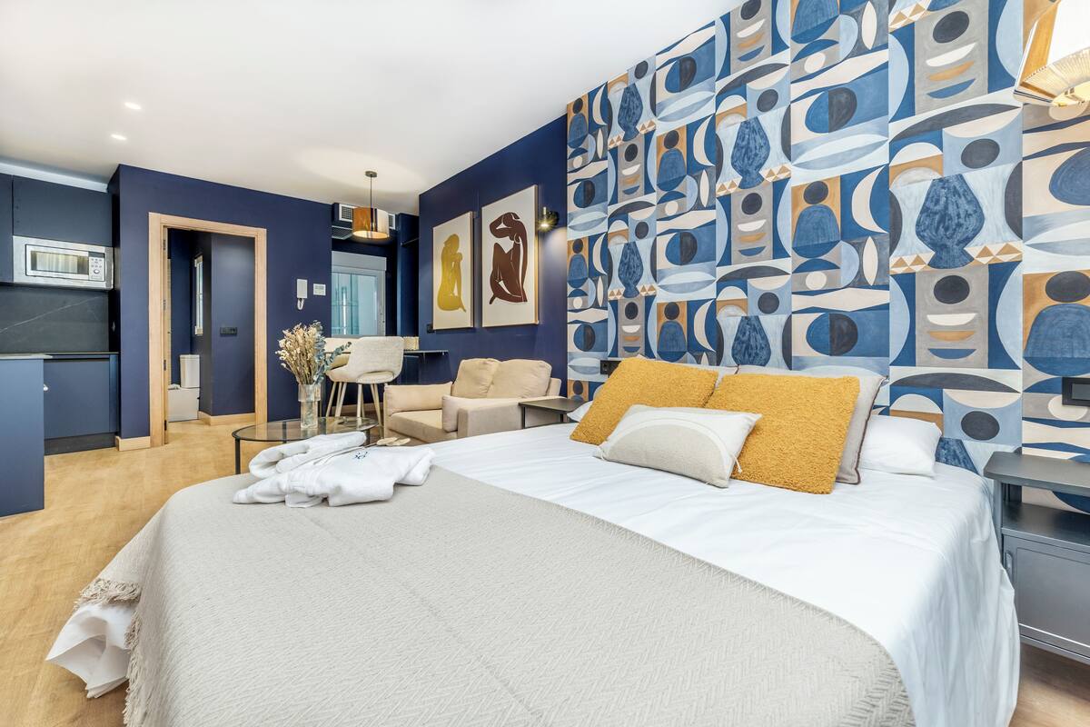 Une chambre d’hôtel moderne avec un grand lit, un bureau, une chaise et un mur décoré d’œuvres d’art abstraites.
