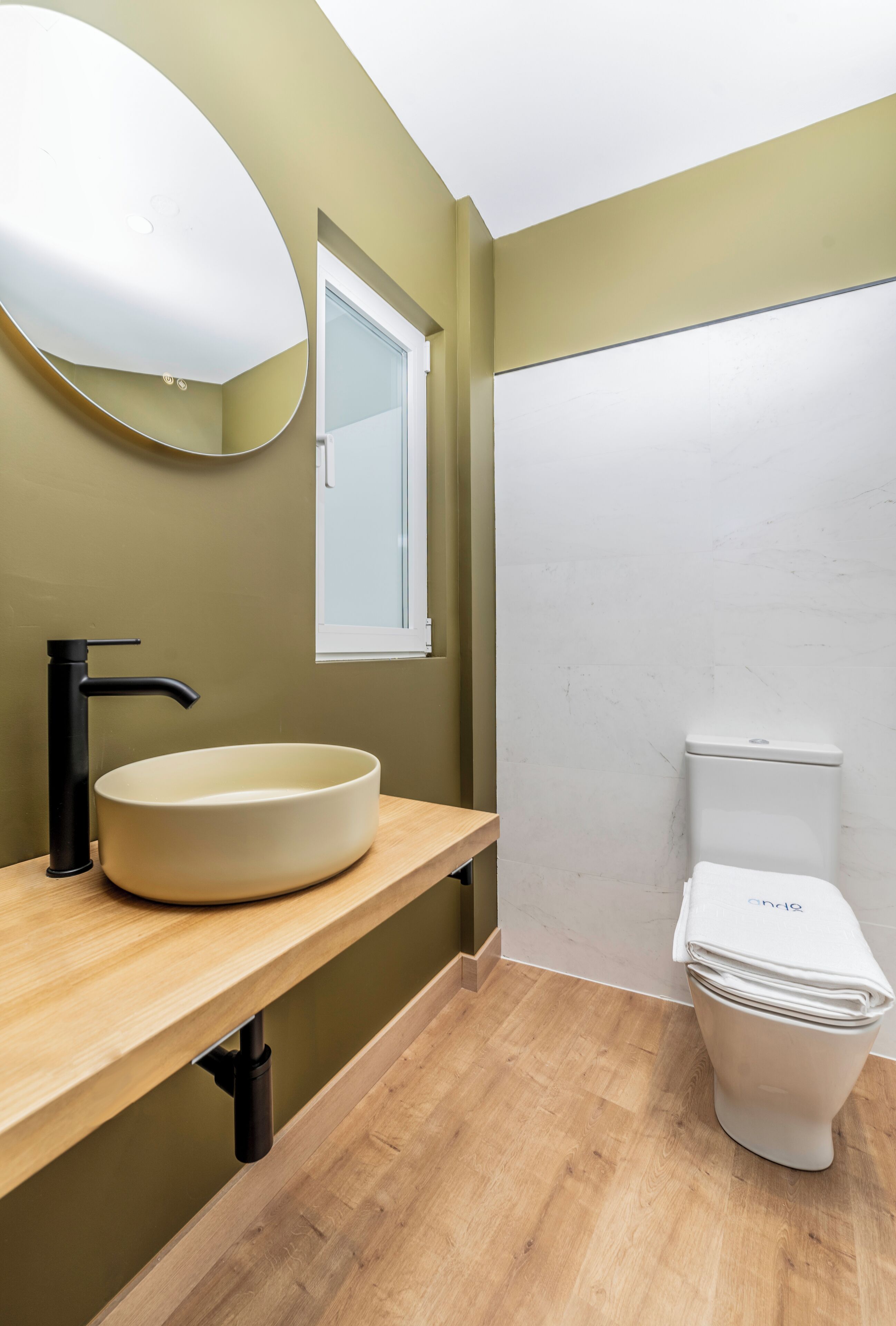 A bathroom with a round sink, black faucet, and a toilet.