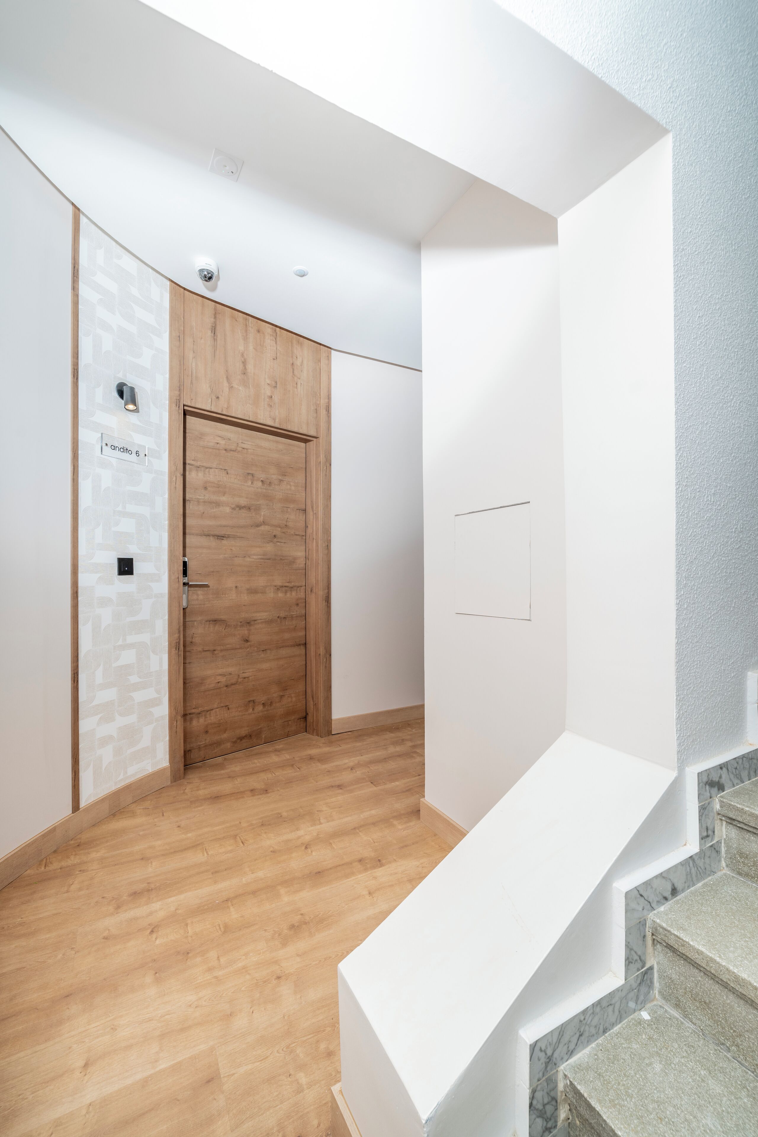 A modern interior with a wooden door, a white wall with a geometric pattern, and a marble staircase.