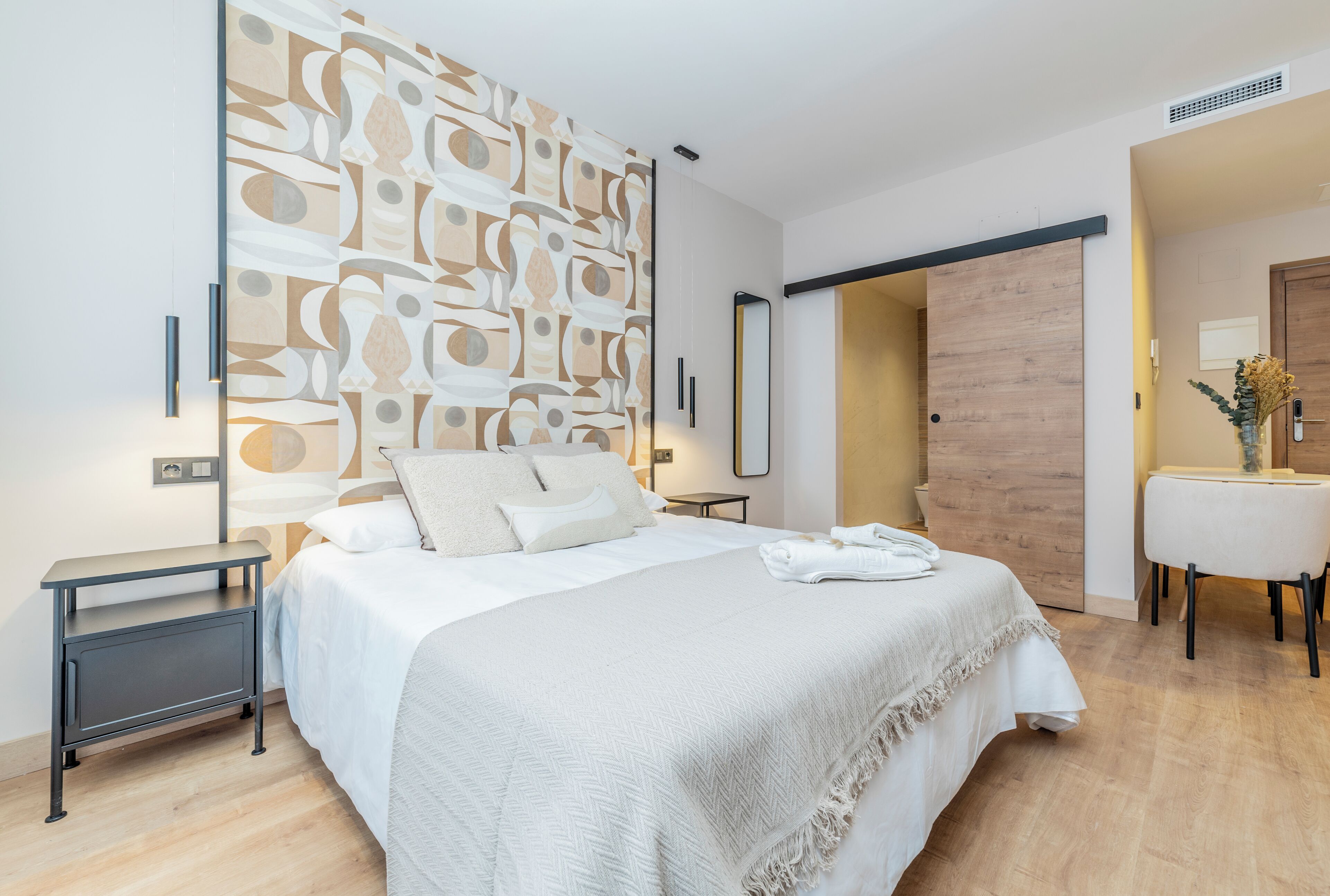 A modern bedroom with a large bed, bedside tables, a wall art piece, and a wooden door.