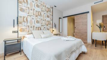 A modern bedroom with a large bed, bedside tables, a wall art piece, and a wooden door.