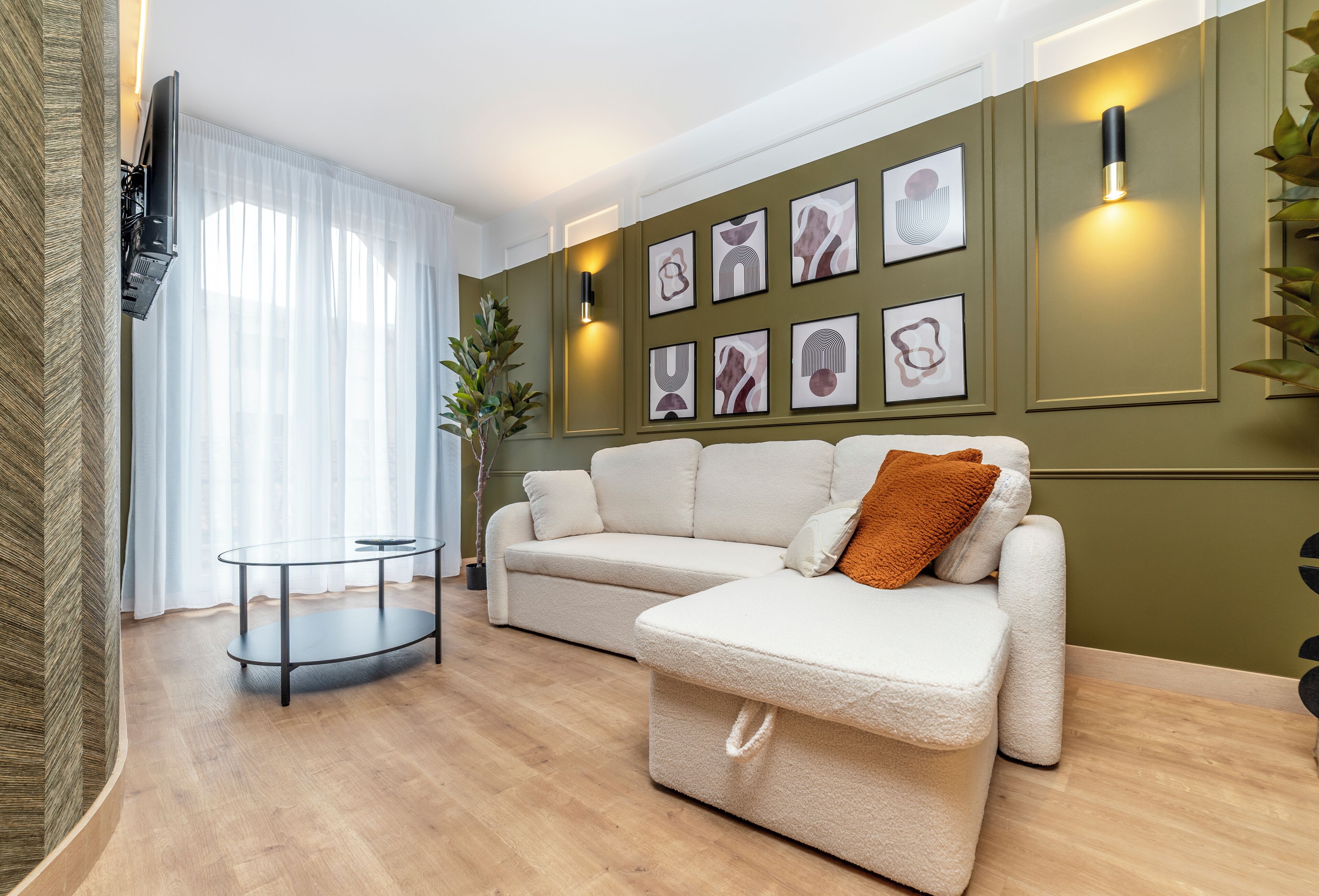 Una sala de estar moderna con un sofá, una mesa de centro de vidrio y un televisor montado en la pared.