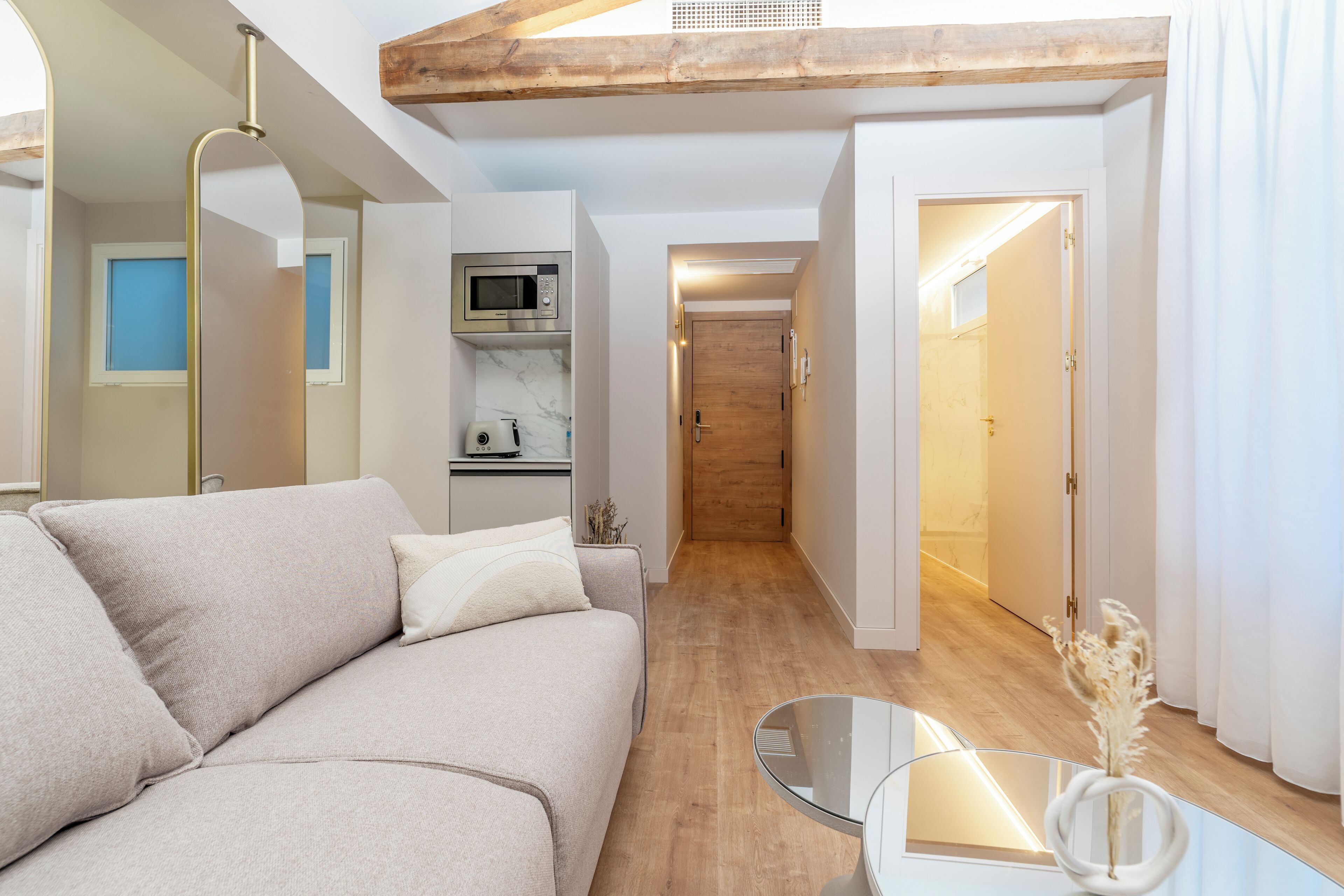 Una sala de estar moderna con un sofá, una mesa de centro de vidrio, un microondas y una puerta de madera que da a otra habitación.