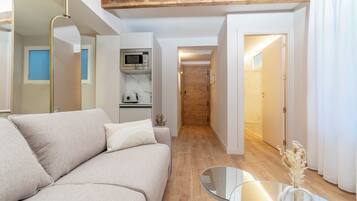 Una sala de estar moderna con un sofá, una mesa de centro de vidrio, un microondas y una puerta de madera que da a otra habitación.