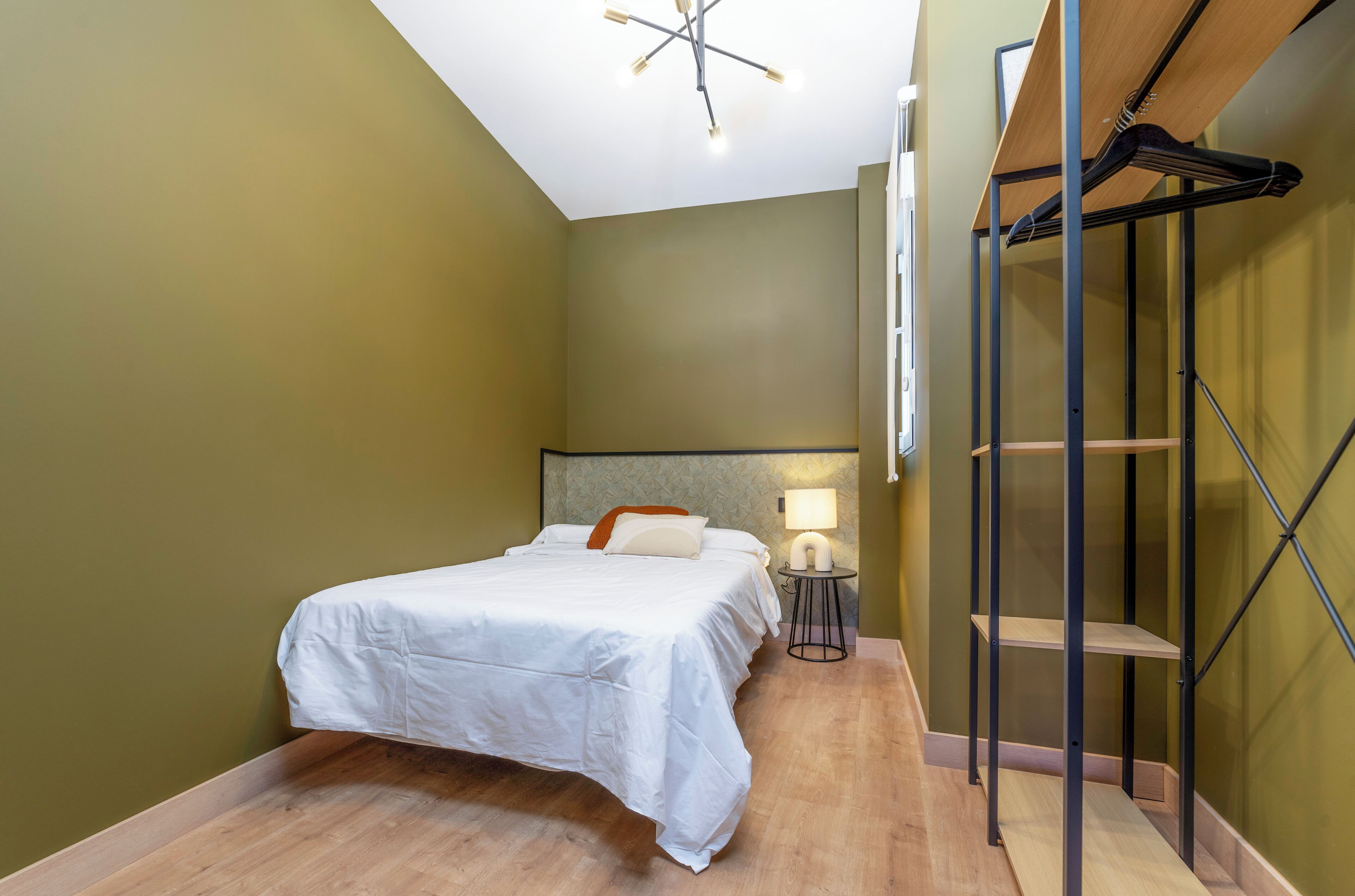 Un dormitorio con cama, lámpara de noche y suelo de madera.