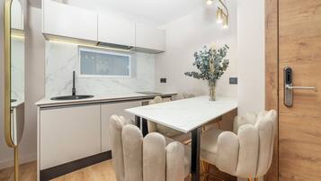 Une cuisine moderne avec des meubles blancs, un pare-feu en marbre, une fenêtre intégrée et un coin repas comprenant une table blanche et des chaises rembourrées.