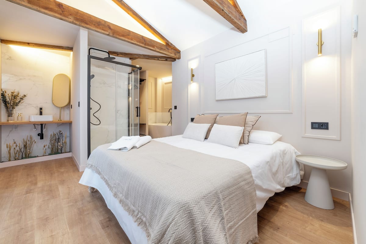 Une chambre moderne avec un grand lit, des tables de chevet, une douche en verre et un mur en marbre.