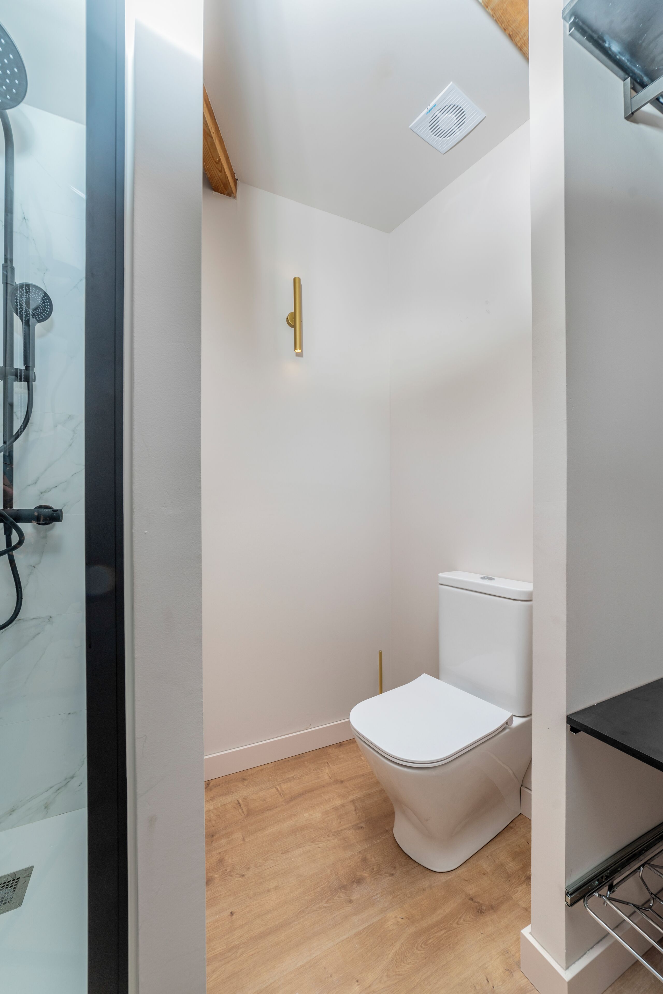 Un baño con inodoro blanco, ducha y suelo de madera.