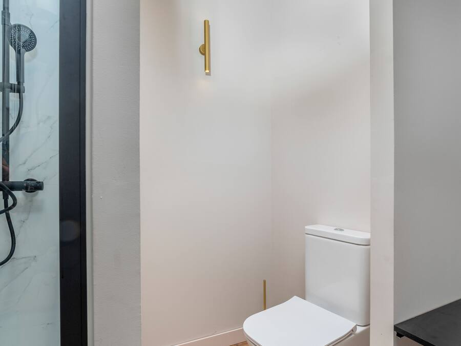 Un baño con inodoro blanco, ducha y suelo de madera.