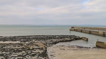 A coastal view with a concrete pier extending into calm waters, a rocky beach area, and a distant shoreline.