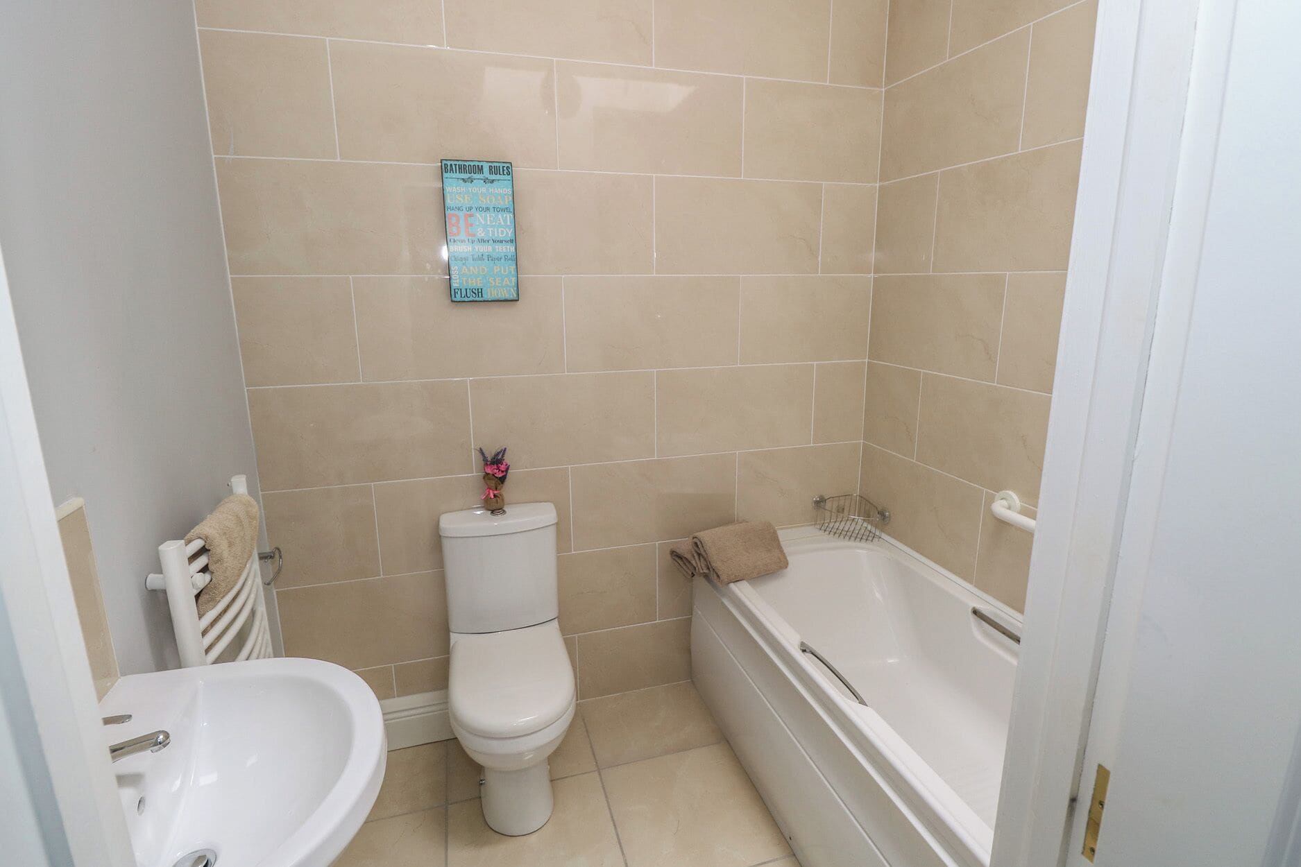 Un bagno con water, lavandino e vasca. Sul muro è affissa una segnaletica con le regole del bagno.