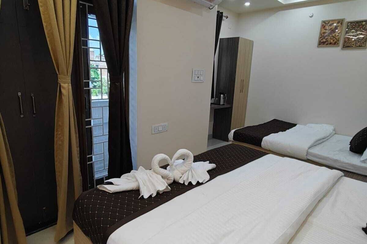 Habitación de hotel con dos camas, un ventanal grande con cortinas, un aire acondicionado y un ventilador de techo, además de un mueble pequeño.