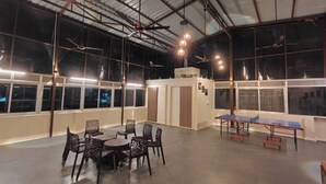 A spacious indoor area with a ping pong table, chairs, and ceiling fans. - Glow Inn HomeStay (Varanasi)