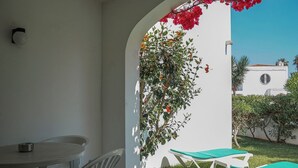A patio with a table and chairs, a covered seating area, and a white wall with a red flower archway. - Quentao Red Villa, Quarteira, Algarve (Quarteira)
