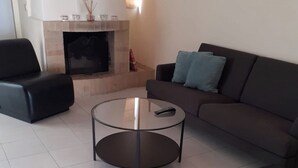 A living room with a fireplace, a sofa, a coffee table, and a black armchair. - Quentao Red Villa, Quarteira, Algarve (Quarteira)