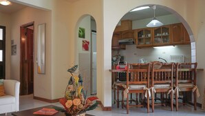 A spacious living area with a dining table and chairs, a kitchen visible through an archway, and a decorative plant centerpiece. - Quentao Red Villa, Quarteira, Algarve (Quarteira)