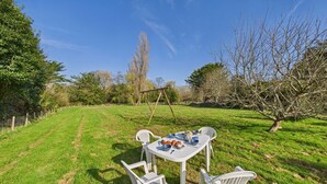 A grassy outdoor area with a table set for a meal, surrounded by white plastic chairs. - House in La Torche - Large garden for 4 (Saint-Jean-Trolimon)