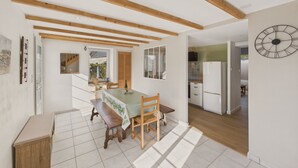 A spacious kitchen with wooden beams, a dining area with a table and chairs, and a large wall clock. - House in La Torche - Large garden for 4 (Saint-Jean-Trolimon)