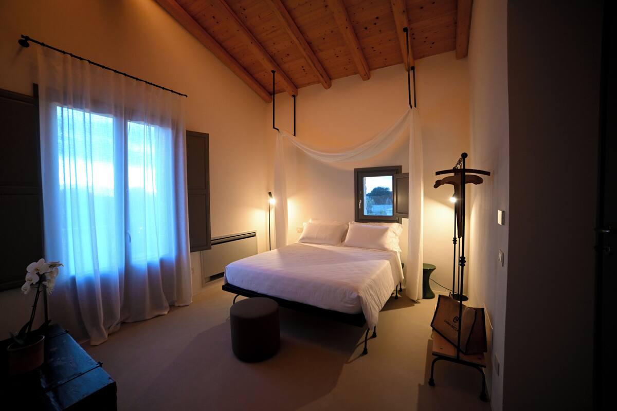 Une chambre à coucher avec un lit, une fenêtre avec des rideaux, une table de chevet et une commode.