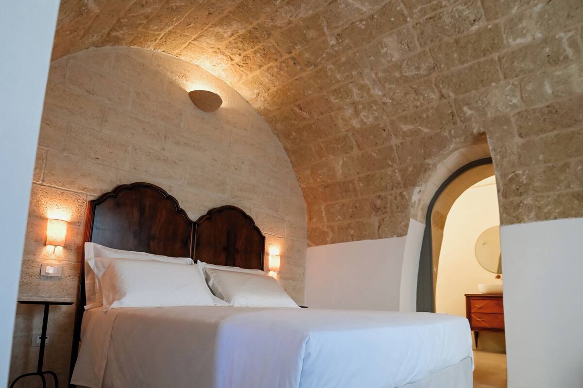 Une chambre avec un plafond en pierre, une tête de lit en bois et un lit blanc.