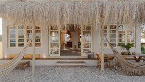 Une structure à toit de chaume, avec une vue sur l’intérieur, notamment sur un coin repas et un hamac.