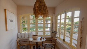 Une pièce chaleureuse avec une table ronde, un canapé et deux fauteuils. De grandes fenêtres offrent une vue sur la verdure environnante.
