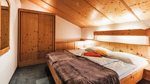 Ein Schlafzimmer mit Holzboden, einem Bett mit brauner Decke, weißen Kissen und einem Holzschrank.