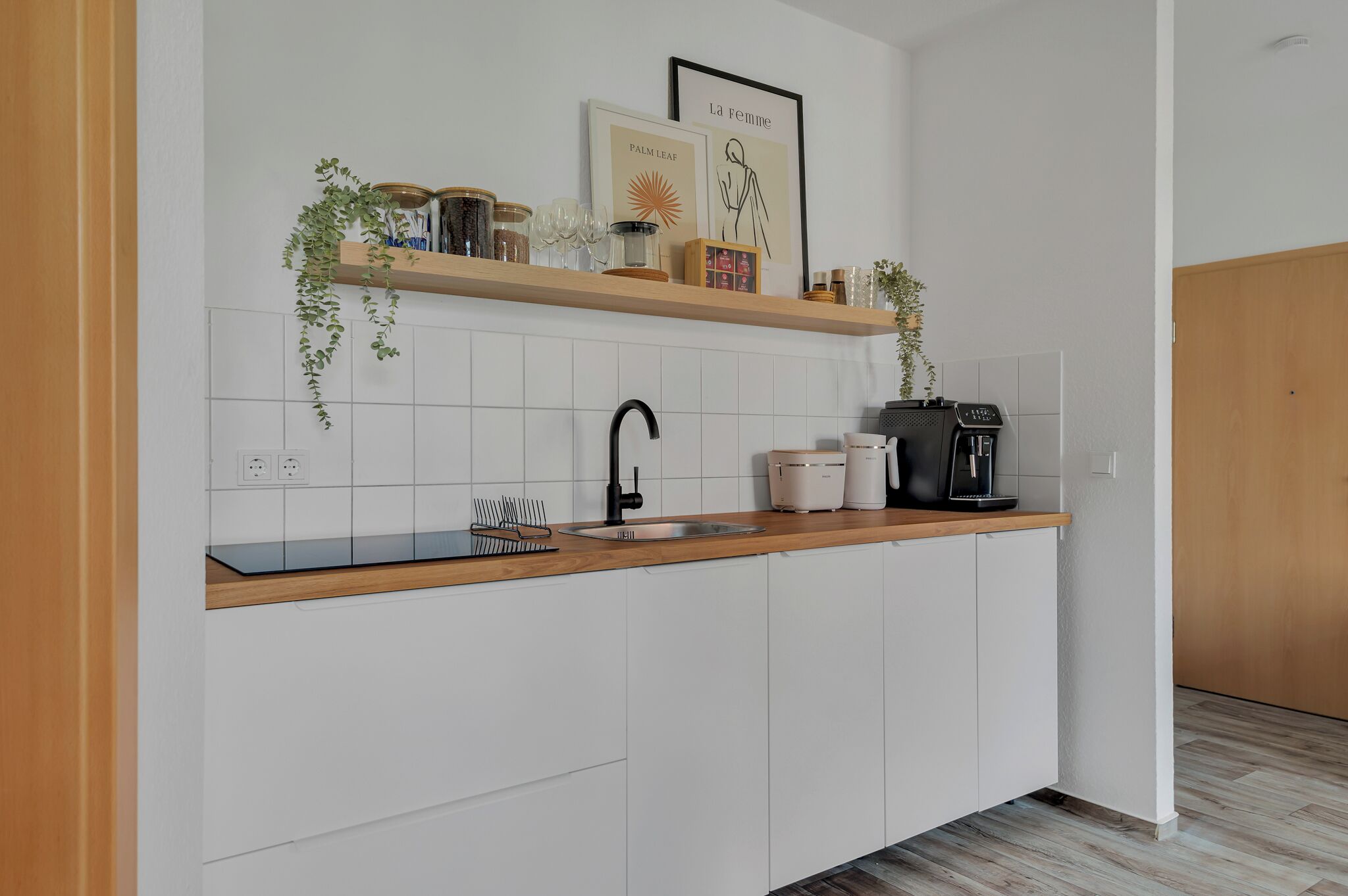 Una cocina moderna con armarios blancos, encimera de madera, grifo negro y cafetera.