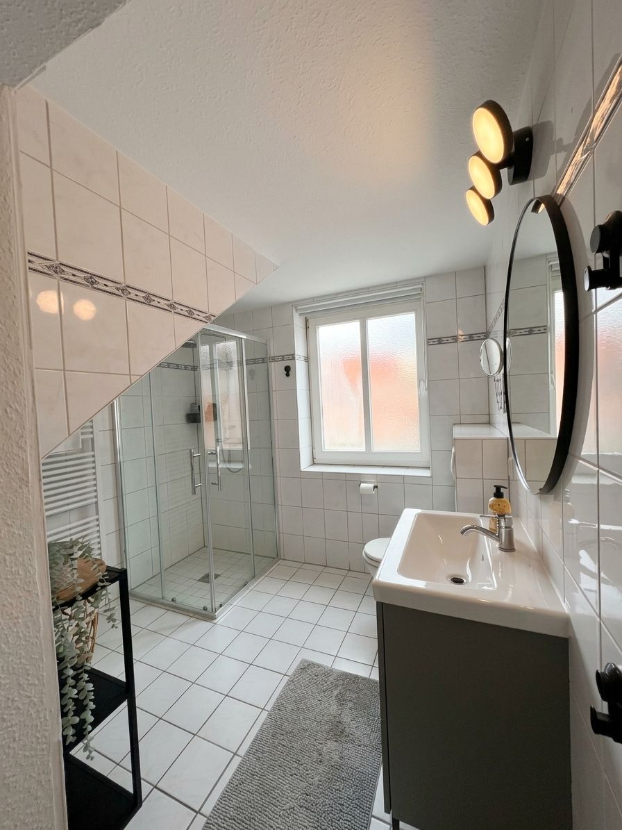 A modern bathroom with a glass shower enclosure, a white sink, and a large mirror.